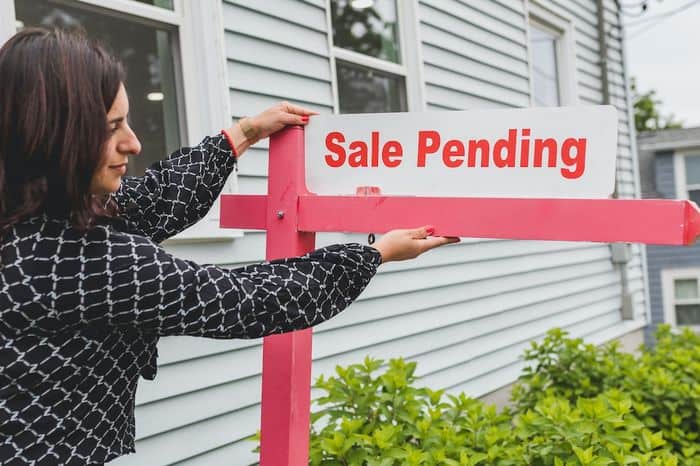 Woman positioning a House Sale pending sign in front of a house.