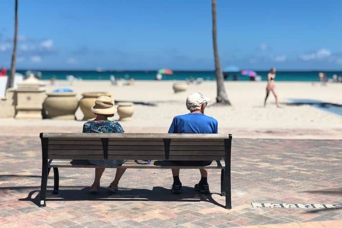 A retired couple sat on a promenade bench by the sea and beach.
