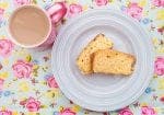 Slices of Lemon Drizzle Cake on a floral background next to a mug of tea.