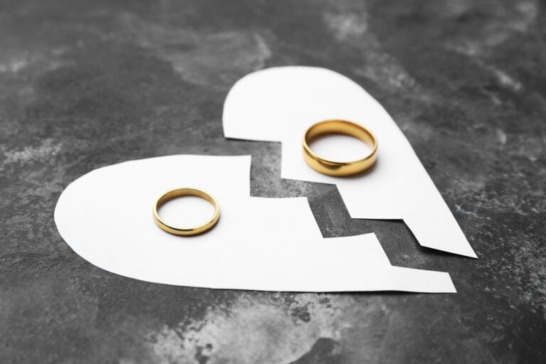 Two gold wedding rings placed on a broken paper heart, symbolising the emotional toll of dealing with a nasty divorce.