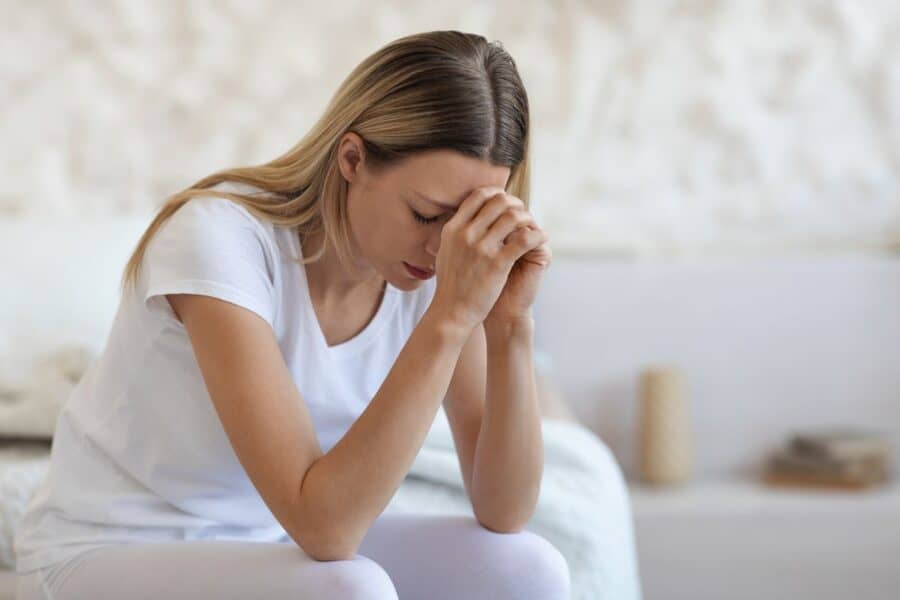 A distressed woman sitting on a bed with her head in her hands, illustrating the emotional stress of dealing with a nasty divorce.