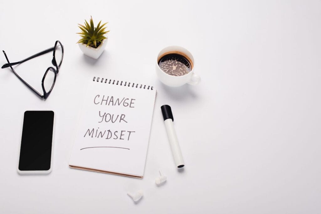 Notebook saying change your mindset beside coffee, phone and glasses.
