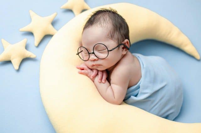 A newborn baby sleeping on a moon shaped pillow