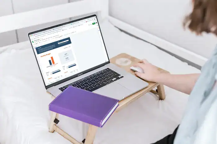 Woman managing family finances on her laptop open to her monthy budget page, with a purple notebook.