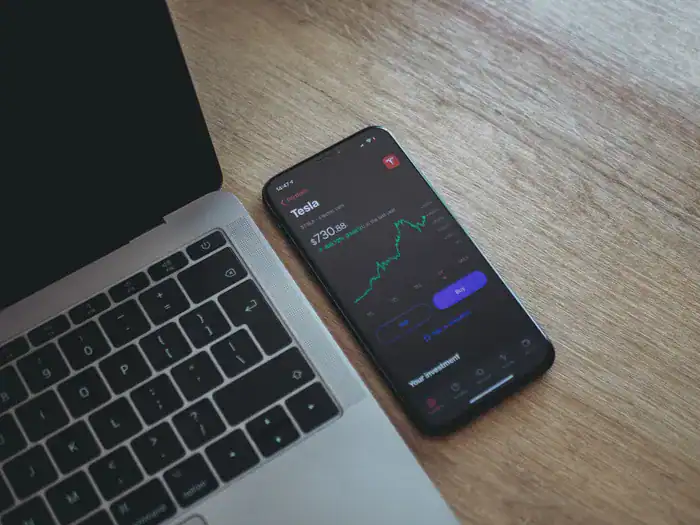 A mobile phone next to a laptop showing the share price of an investment in Tesla shares.