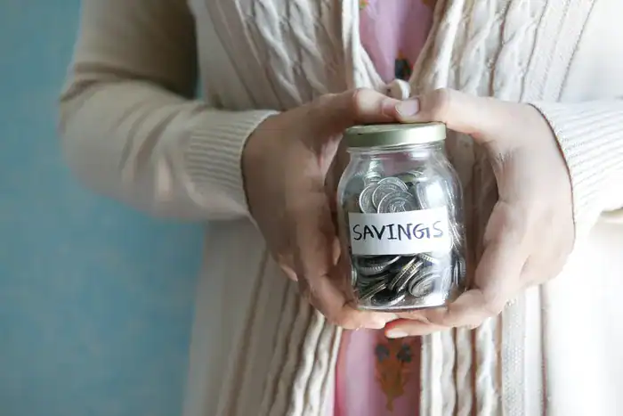 Someone holding a jar of money with a label stating savings on it.
