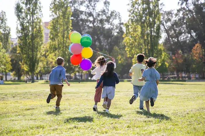 Children running away from camera with a bunch of balloons.