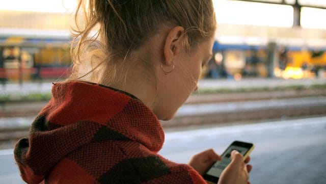 A teenager with a phone on a train platform
