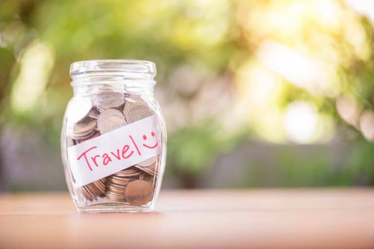 Glass jar filled with coins labelled 'Travel' – symbolising simple ways to save money while travelling.