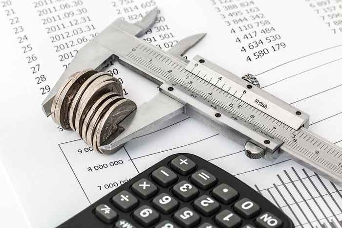 coins in the mouth of a wrench with a calculator and budget form
