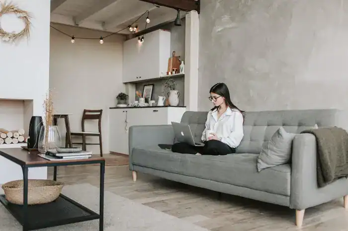 Student sat crossed legged with a laptop on a nice sofa in a nice house for students off campus.