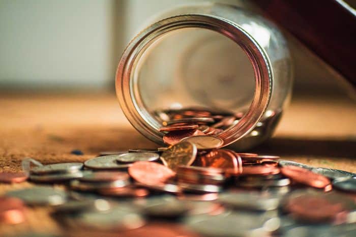 coins scattered around a glass savings jar