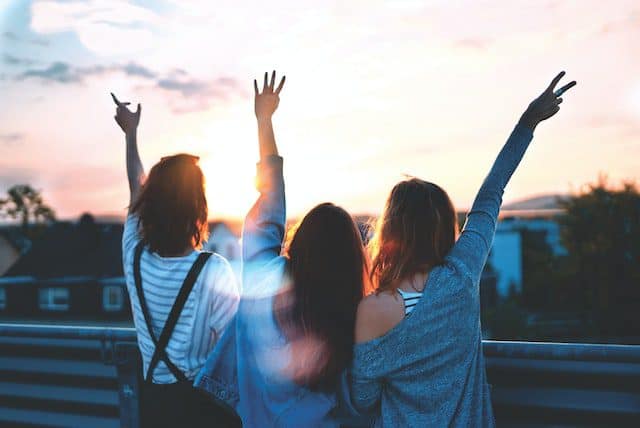 university friends living off campus stood with their backs to the camera and their arms in the air
