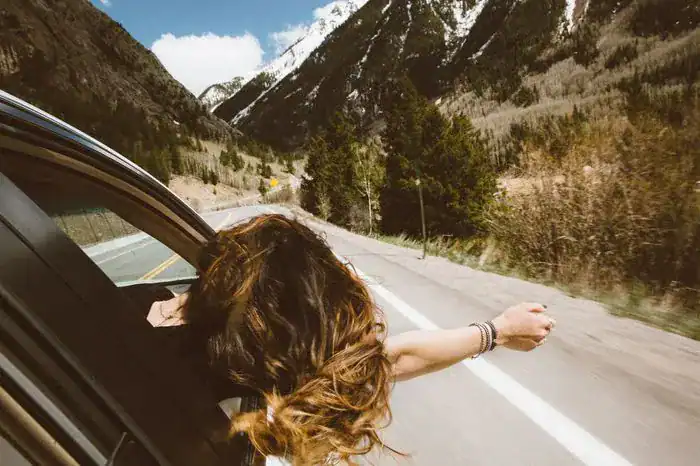 Woman sticking her head and arm out of a moving car along a quiet road.