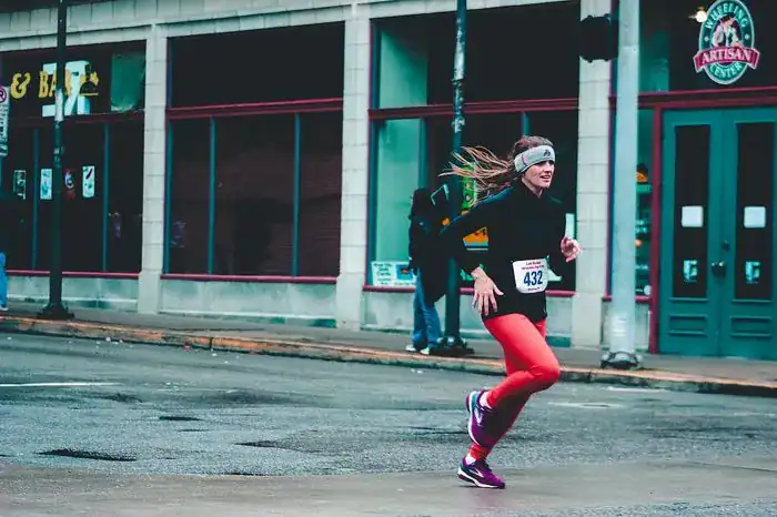 Woman wearing orange running tights and running shoes running along the road in a race.