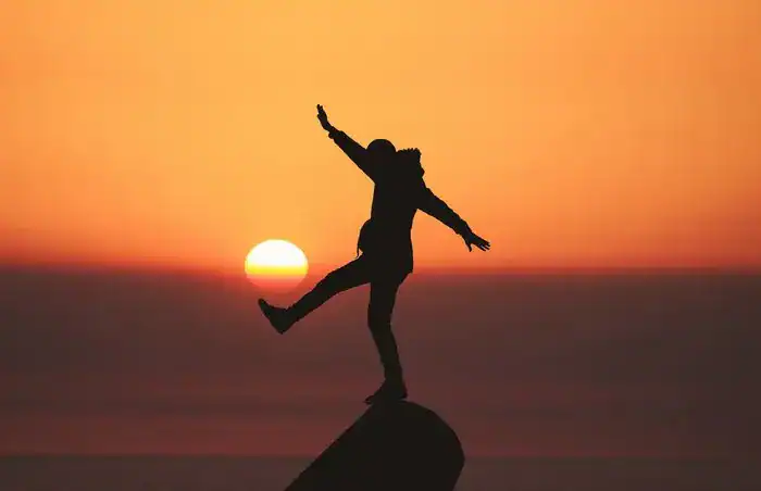 Someone standing on a rock with a bright orange sunset behind them.