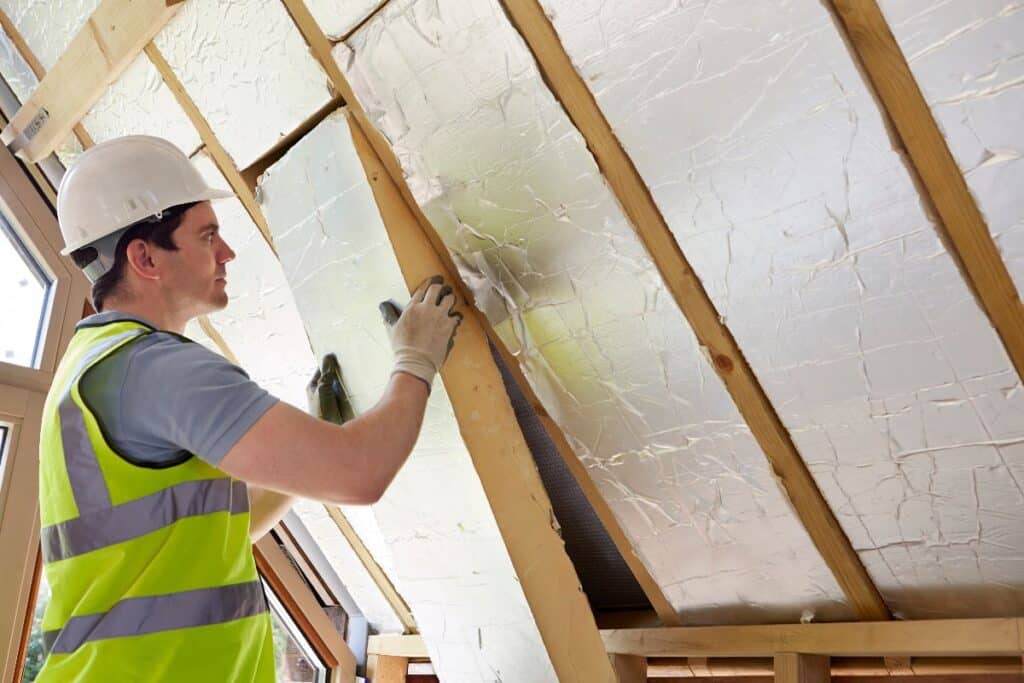 Installer fitting rigid boards under loft rafters to save energy with insulation.