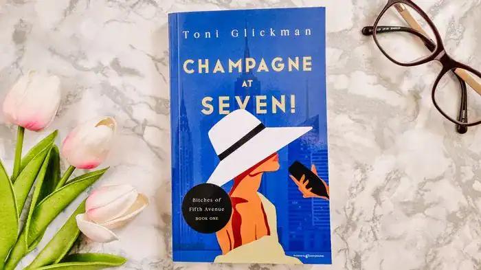 Champagne At Seven book cover on a flatlay with flowers and a pair of glasses.