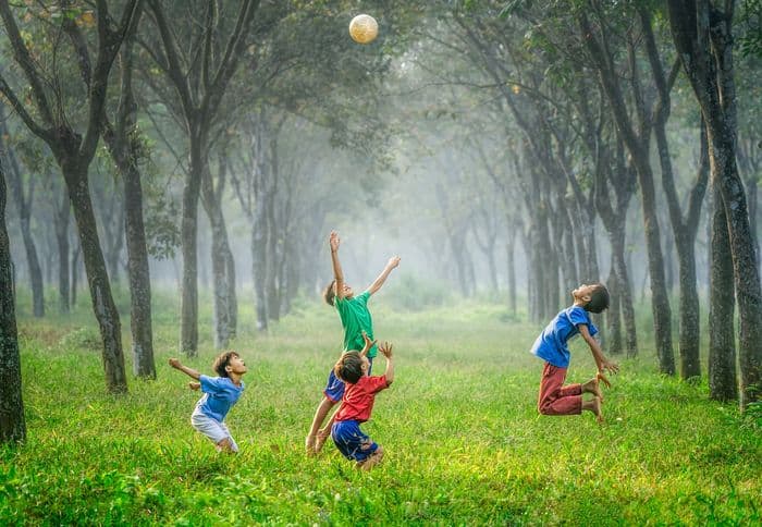Kids playing with a ball in the air, in woodland.