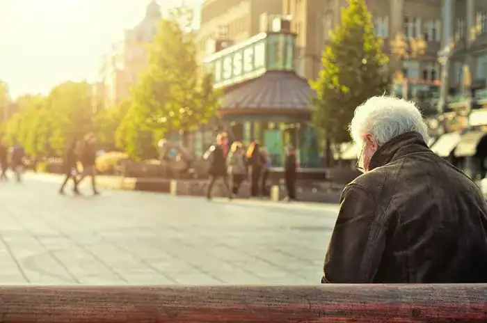 Old man sat on a bench in a town centre.