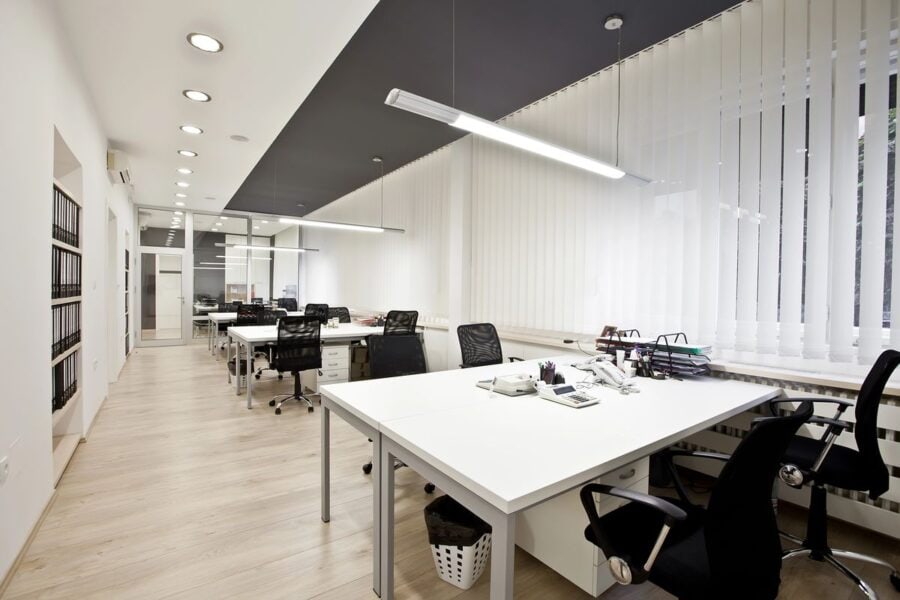 A modern office space with desks, chairs, and organised shelves.