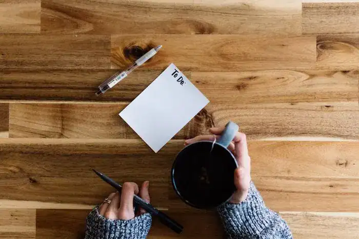 Someone holding a mug of coffee sat at a table with a to-do-list and pen.