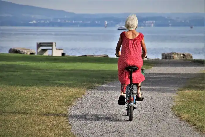 Old woman wearing a red dress and riding a bike by the sea.