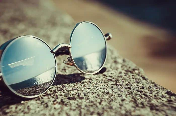 Round sunglasses for a square face shape, resting on a wall by the beach.
