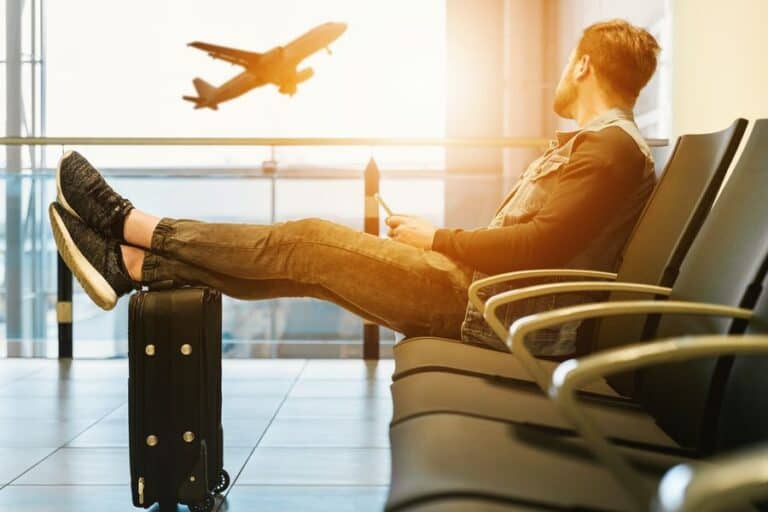 Man sat in an airport with his feet rested on his suitcase staying connected when travelling by using his mobile phone.