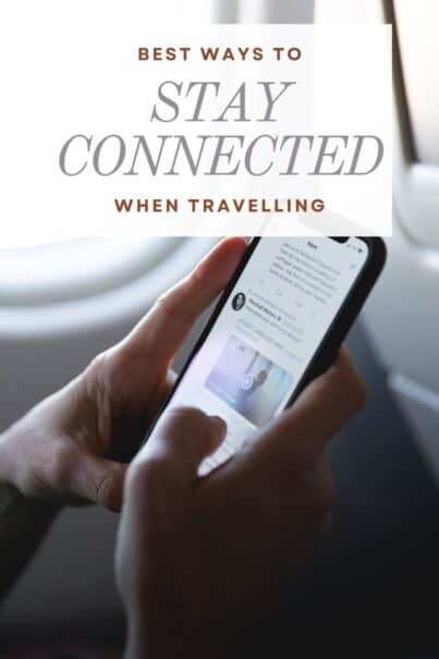 Someone holding up and scrolling through a mobile phone up by an airplane window.