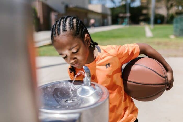 Child holding a basketball, staying hyrated by drinking for a water fountain.