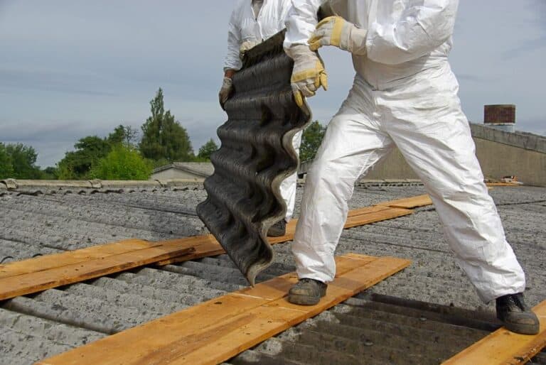 Men in hazmat suits removing asbestos lined roofing after asbestos surveys completed.
