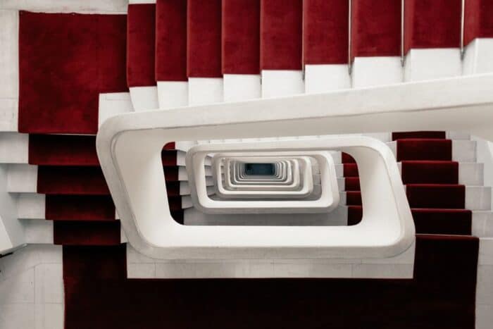 L shaped staircases with a red carpet and white paint outer section and bannister.