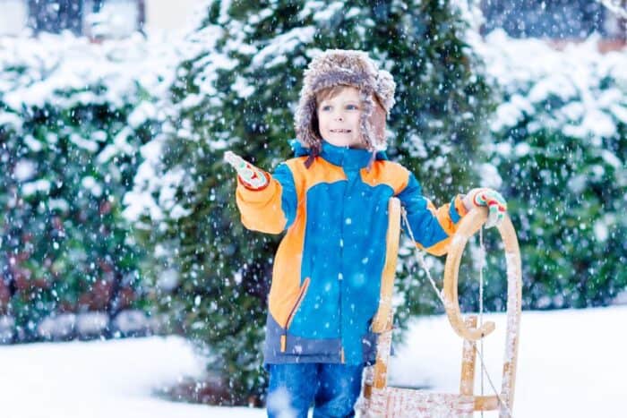 Boy in a blue coat and wearing a hat, holding a sledge and getting ready to have fun in the Christmas snow,