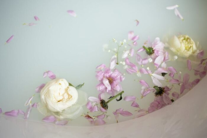 Milk bath water with flowers floating on top to give them impression of what milk bath nails would look like as an elegant beauty trend.
