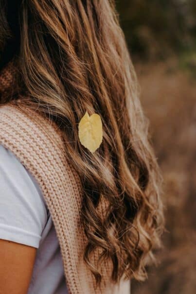 The image captures the back view of a woman showcasing a Scandi hair look. She has long, naturally wavy, reddish hair that cascades down her back in effortless waves. The hair's texture is highlighted by the soft lighting, emphasizing the natural volume and flow. The focus on her hair against a simple, uncluttered background accentuates the beauty of the Scandi style, characterized by its simplicity and elegance. The woman's posture and the hair's arrangement convey a sense of casual grace, typical of Scandinavian beauty aesthetics.