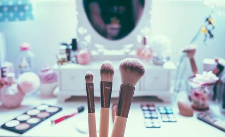 A range of makeup and skincare products laid out on a table as someone holds up makeup brushes, taking a look at the latest beauty trends for the year.