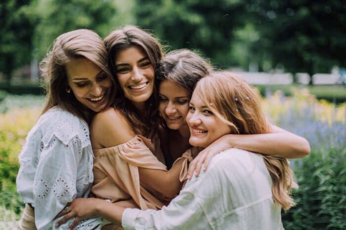 Four joyful women hugging and smiling in a garden, with a soft focus on the vibrant greenery around them, capturing a moment of friendship and happiness.