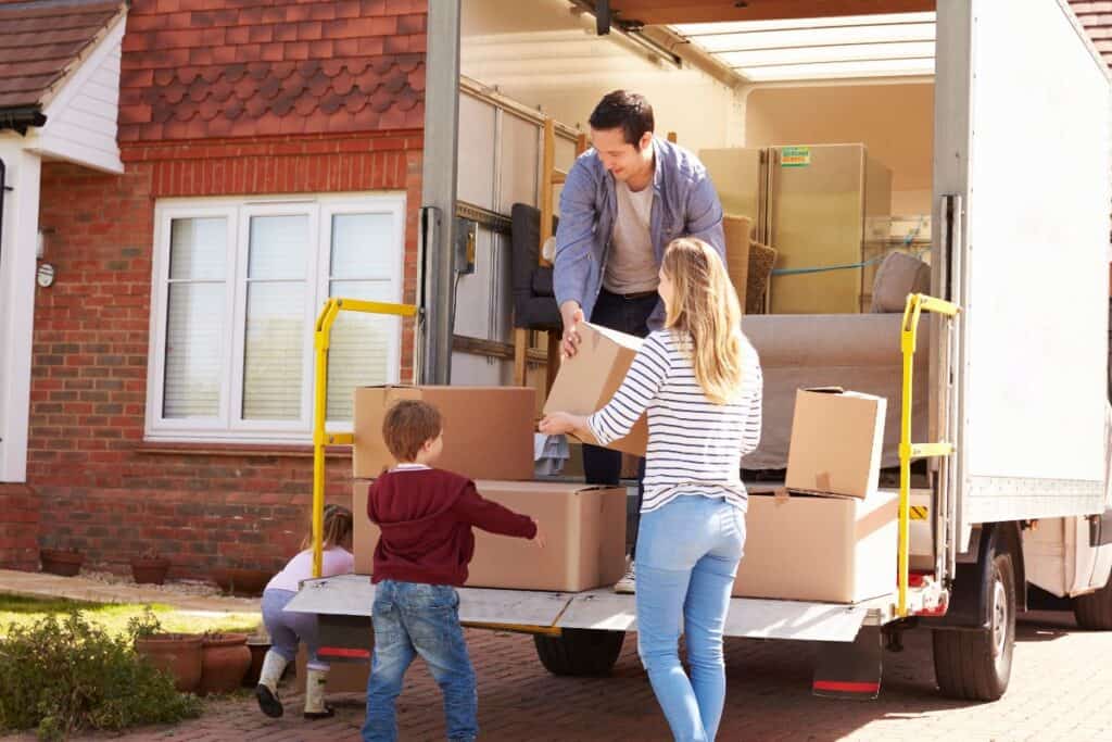 Family loading cardboard boxes into a removal van outside their home when moving house in the UK.