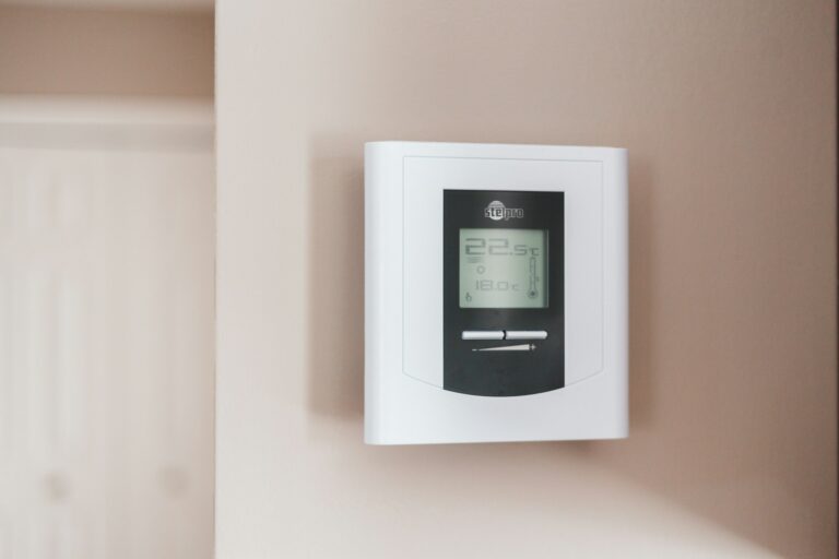 Digital wall-mounted thermostat displaying a room temperature of 22.5 degrees Celsius and a set temperature of 18.0 degrees Celsius, with the 'Heatpro' logo at the top, indicating heating control in a care home environment.