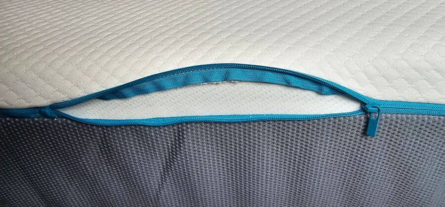 Partially unzipped blue zipper on a textured SIMBA mattress topper, highlighting the product's easy-to-remove cover feature for cleaning or comfort adjustments.