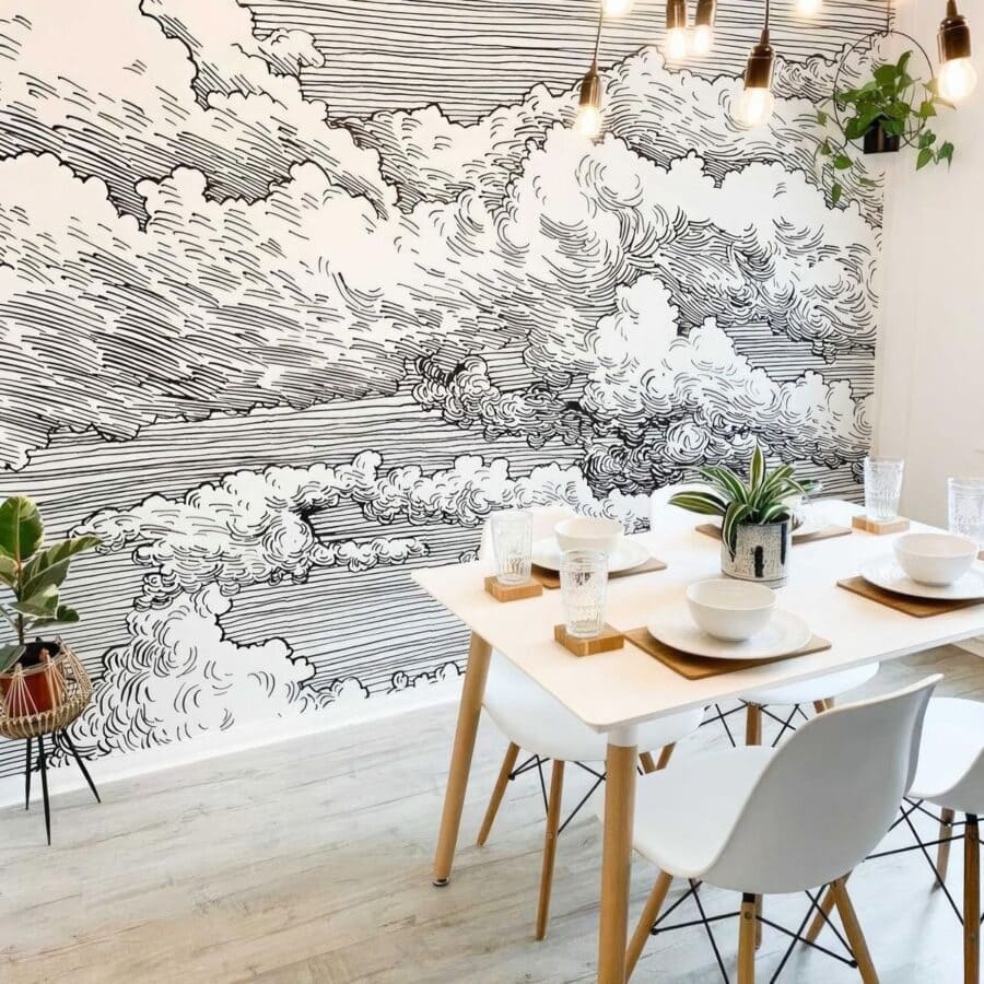 A modern dining area is transformed into a dynamic space with a bold black and white wave-patterned mural, embodying a funky way to personalise your home. The setting is complemented by a minimalist white dining table, contemporary chairs, chic hanging light fixtures and a touch of greenery for a fresh look.