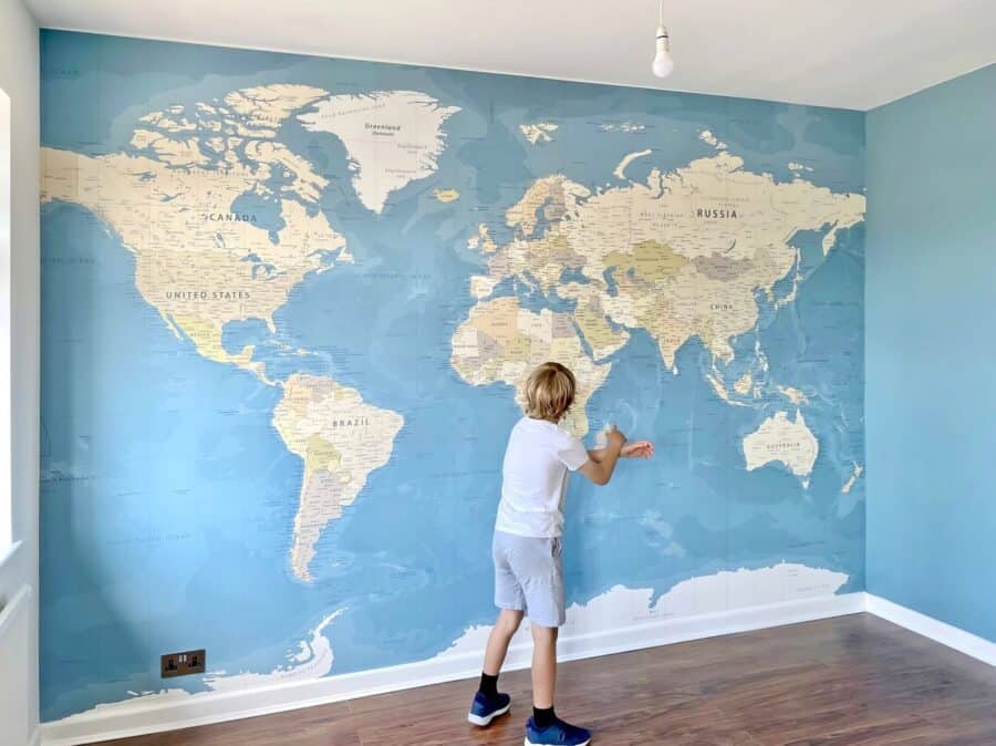A child interacts with a large wall mural of a world map in a light blue room, illustrating a creative way to personalise your home with educational decor.