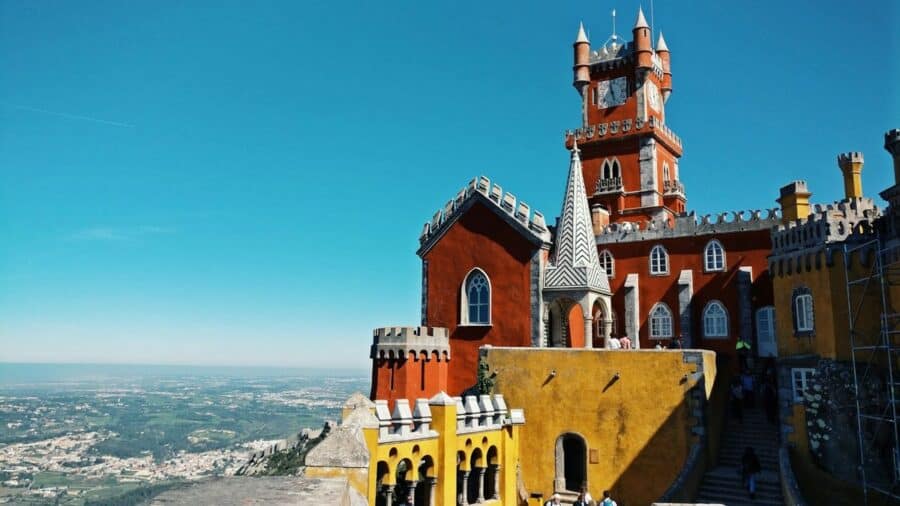 The vibrant colours and unique architecture of Pena Palace in Sintra, Portugal, with its red and yellow facades, ornate towers, and Gothic windows against a clear blue sky.