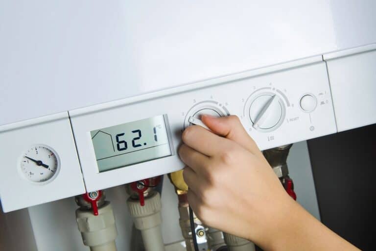 A hand adjusts the temperature dial on a boiler to 62.1°C, showing responsible maintenance to increase the lifespan of your boiler.