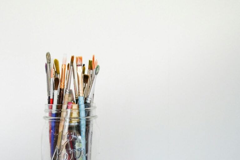 Assorted paint brushes in a clear glass jar set against a plain white background, reminiscent of the artistic tools used in John William Waterhouse paintings. This image sets the stage for exploring the detailed and romantic style characteristic of Waterhouse's works. For a deeper look into a selection of his iconic paintings, click to read the accompanying article.