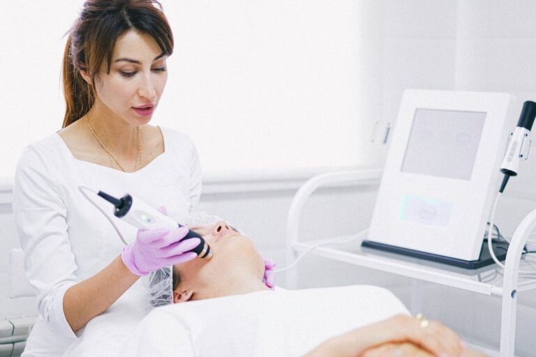 A woman undergoing a CO2 fractional laser resurfacing treatment performed by a professional in a clinical setting. The professional is using a handheld laser device on the patient's face, with medical equipment visible in the background.