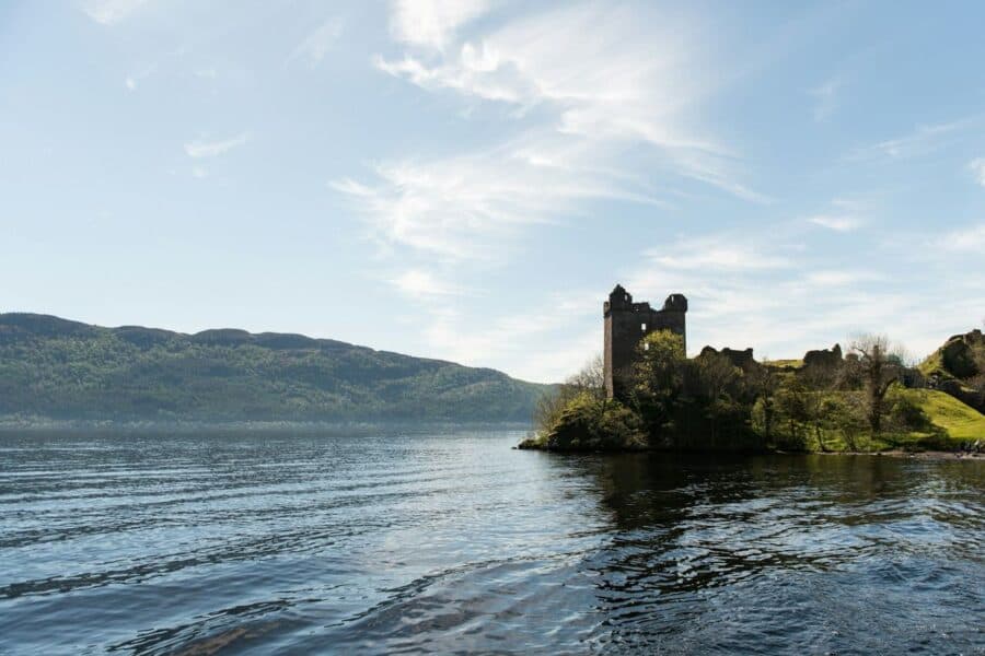Urquhart Castle ruins overlooking Loch Ness with rolling hills in the background and a clear blue sky above. The image highlights accessible travel in Scotland.