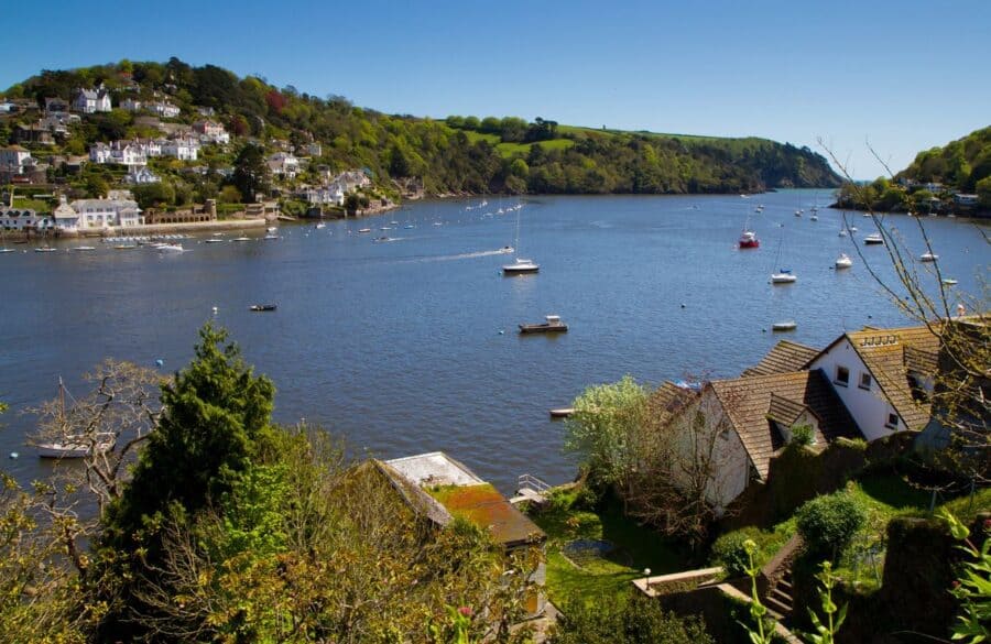 View of the River Dart heading out to sea, with houses nestled along the hillside and various boats anchored on the calm water.