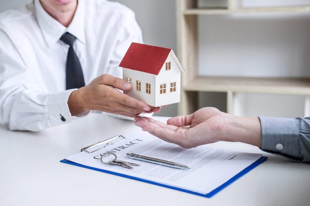 Estate agent handing over a model house above a property contract and keys during a family home purchase